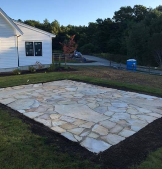 Flagstone patio next to a white house, surrounded by lawn and mulch border.