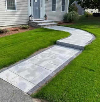 Curving stone walkway leading to a house with a gray door, flanked by green grass.