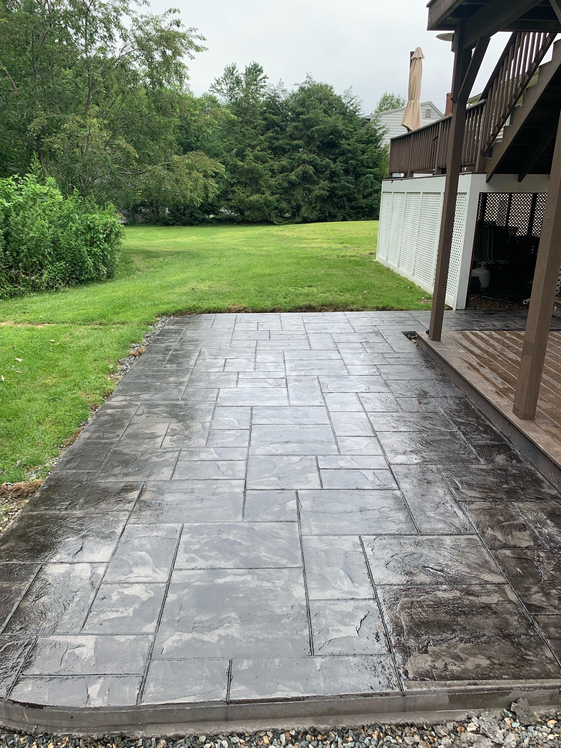 Stamped concrete patio next to a deck, overlooking a grassy yard with trees.