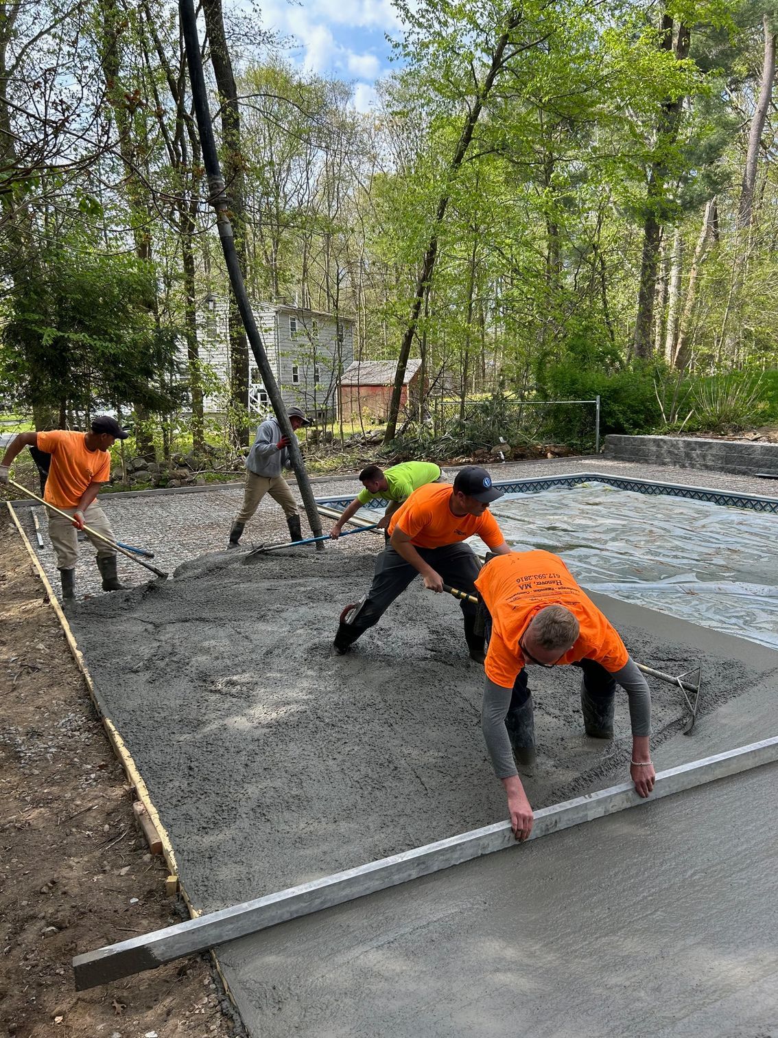 Construction workers pouring and leveling concrete. Outdoors, workers in orange and green shirts.