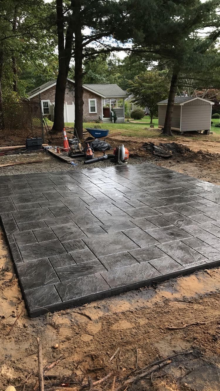 Newly laid dark gray brick patio with tools and a house in the background.