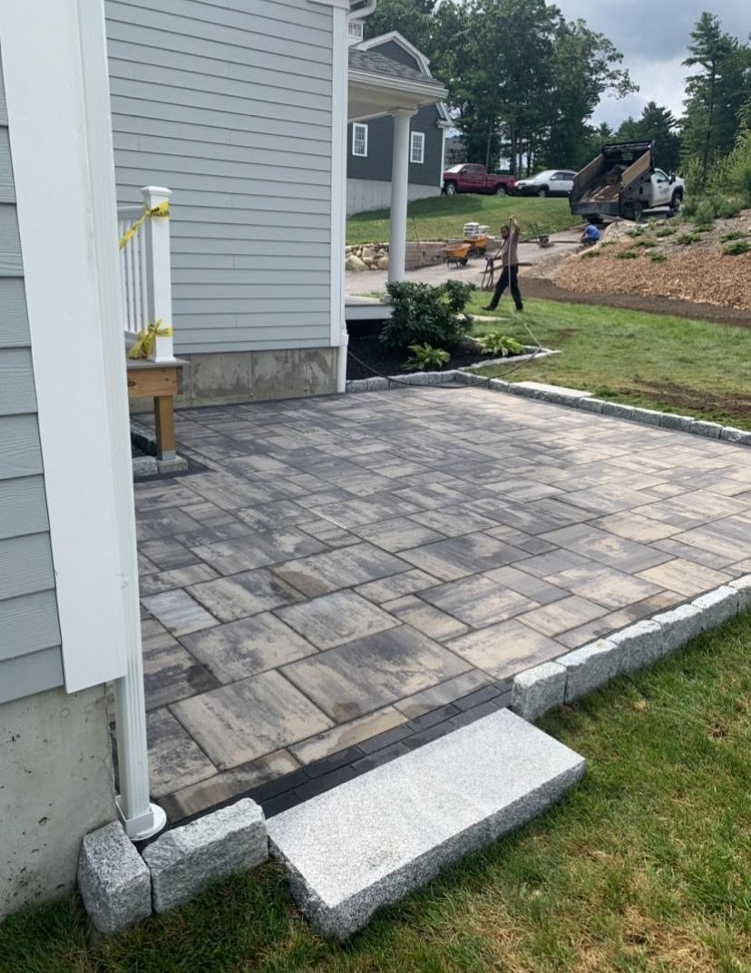 Brick patio next to a house with a small step. A person and truck are in the background.