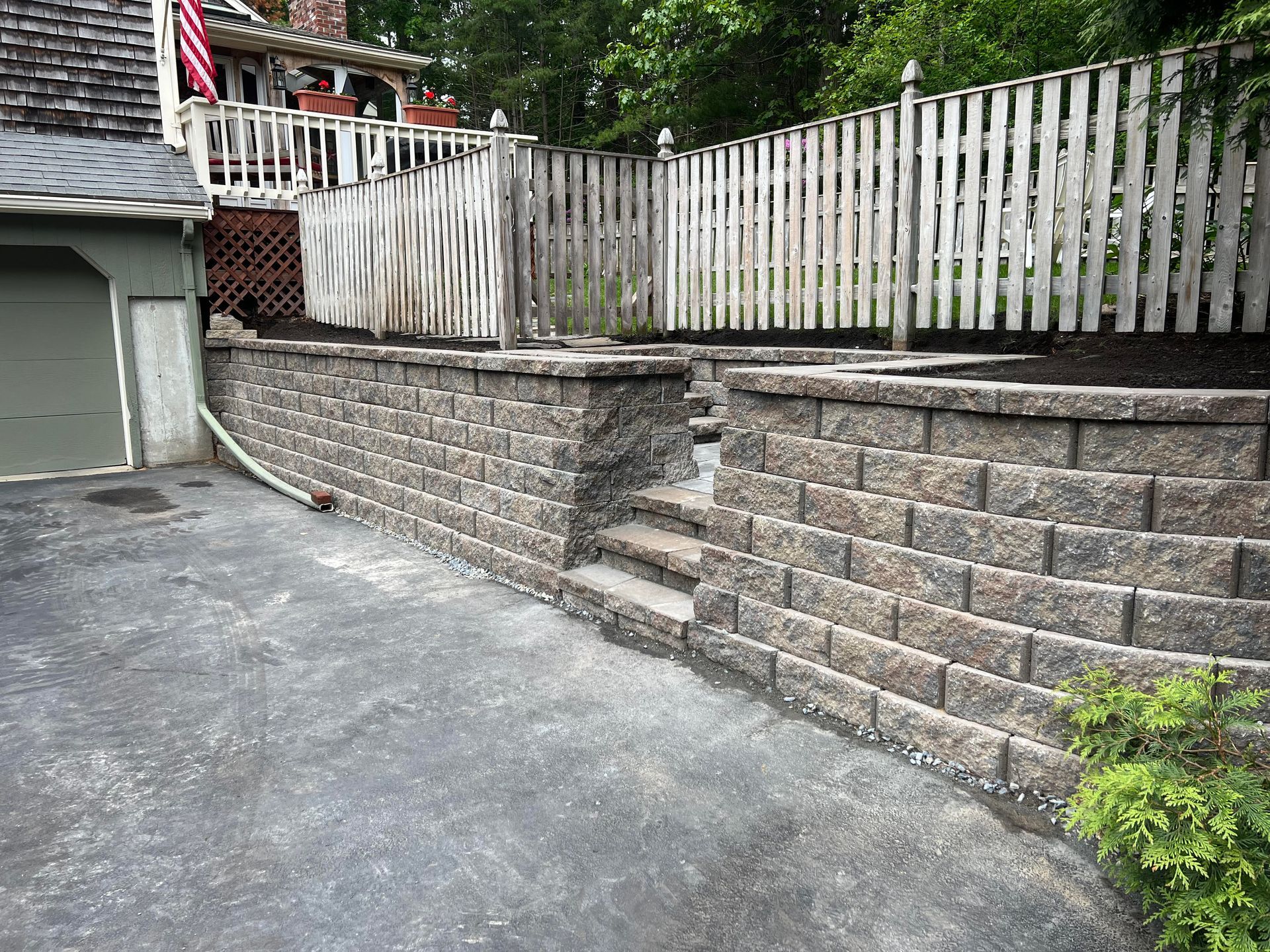 Stone retaining wall with steps, leading to a wooden fence and tiered backyard.