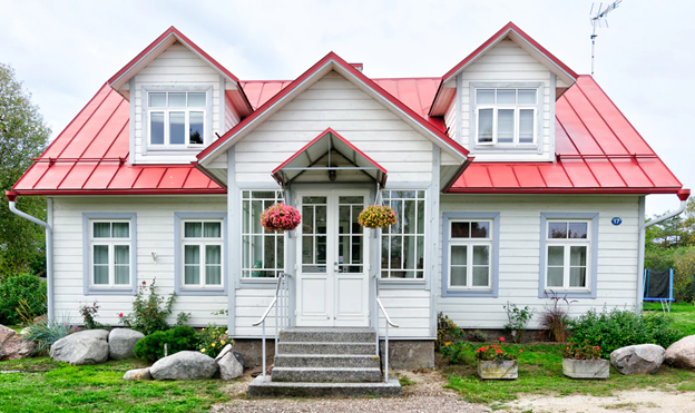 White cottage with red roof, front porch, dormer windows, and hanging flower baskets.