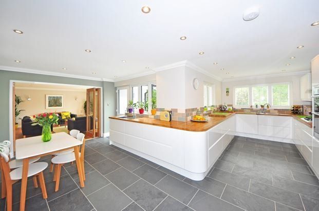 Bright modern kitchen with white cabinets, dark tile floor, and an open dining area leading to a sunlit living room