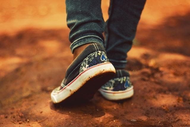 Blue sneakers walking on a dirt path, with one foot stepping forward.