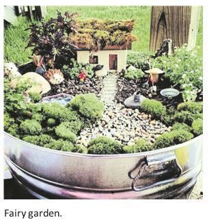 Miniature fairy garden in a metal pot with moss, rocks, tiny house, and small figurines.