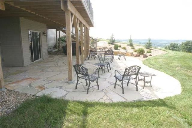 Patio with metal chairs and tables beside a house, overlooking a grassy landscape