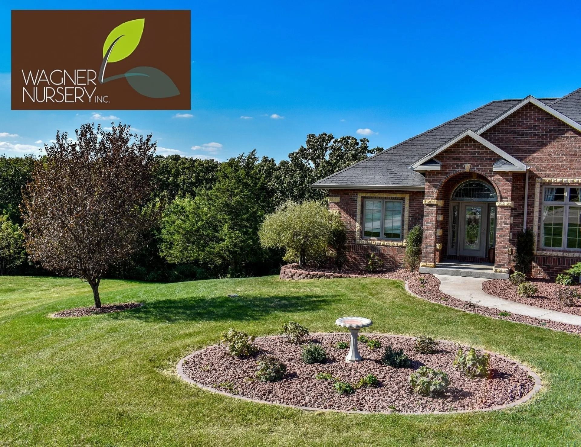 Brick house with manicured lawn, landscaped flower bed, and small tree under a blue sky