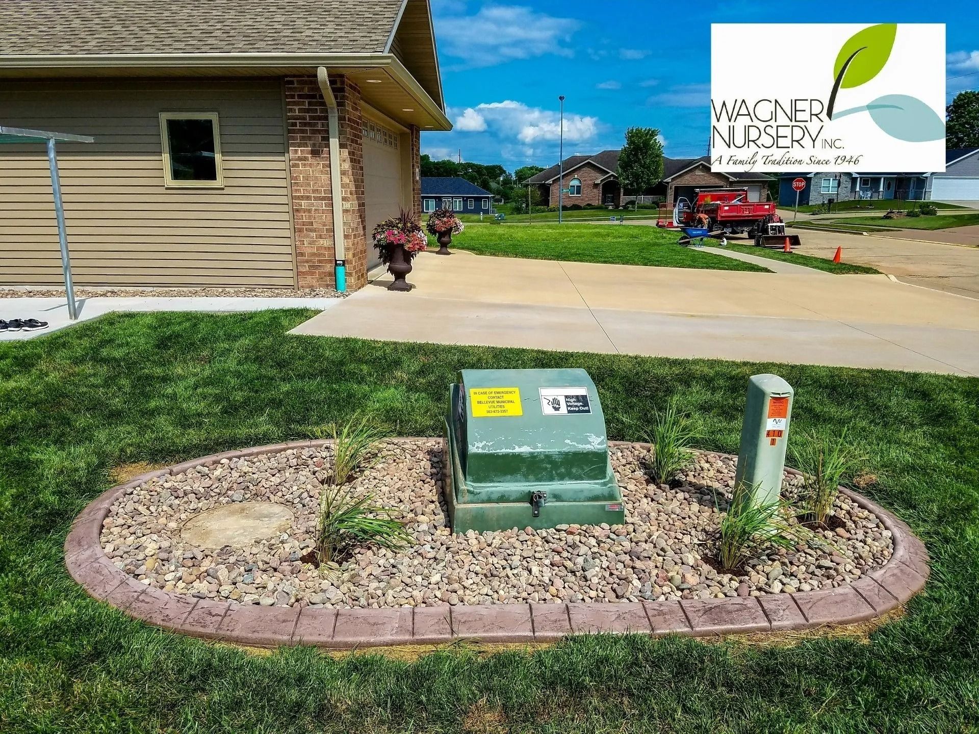 Landscape with utility boxes in a mulch bed by a building and a Wegner Nursery sign.