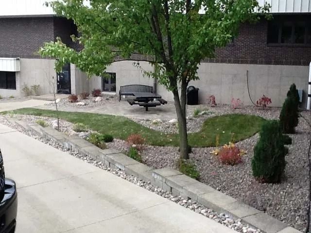 Front yard with gravel landscaping, a tree, shrubs, and a bench beside a house and driveway