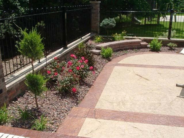 Curved garden bed with blooming pink flowers beside a paved patio and black fence