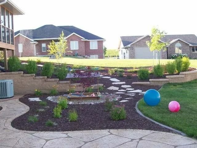Backyard garden with stone path, shrubs, and two colorful balls on the lawn