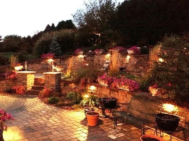 Lit stone steps and flowered terraces in a garden at dusk, with warm lantern lights along the path