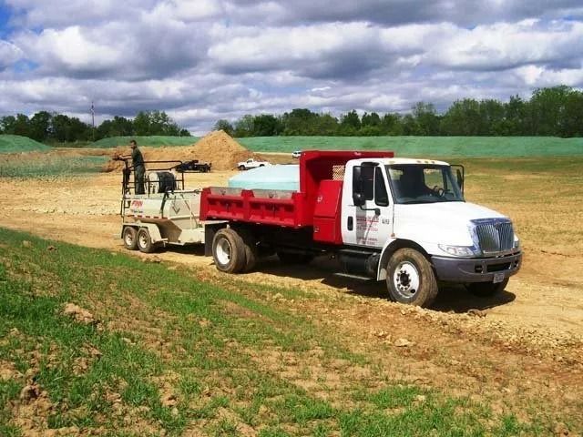 White dump truck hauling a trailer in a field under cloudy sky