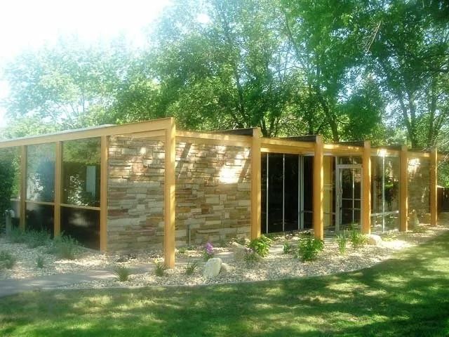 Modern wooden house with glass walls and a flat roof in a sunny wooded setting
