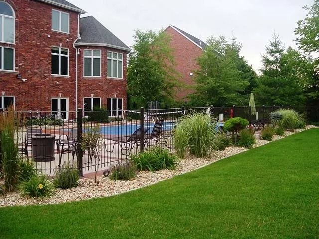 Backyard patio with pool, black fence, and landscaped lawn beside a red brick house