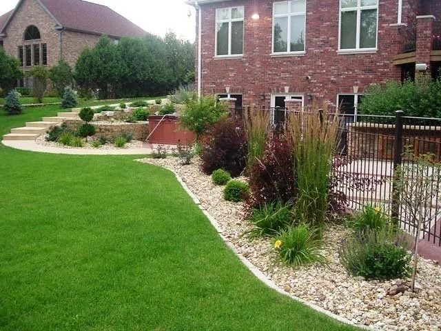 Landscaped backyard with green lawn, stone path, shrubs, and a brick house with patio fencing