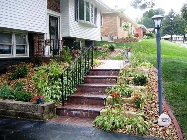 Front yard brick steps with black railings, garden plants, and a lamp post beside a house