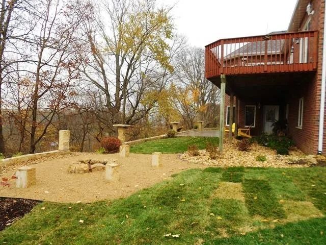 Backyard with gravel patio, small fire pit, deck, and autumn trees beside a brick house