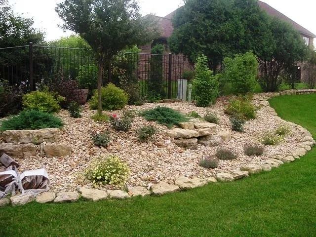 Landscaped garden with rock mulch, shrubs, and a green lawn beside a house
