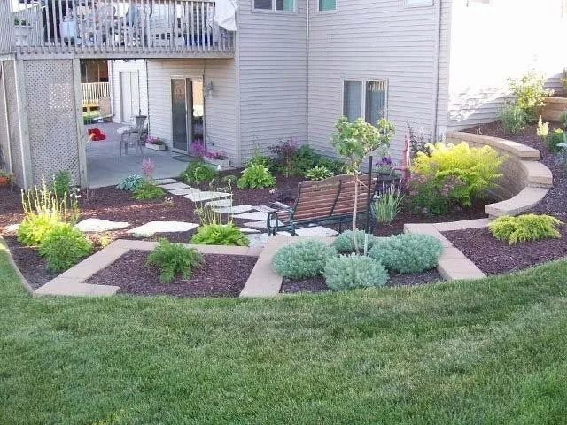 Landscaped backyard with curved stone border, flower beds, lawn, and patio by a house.