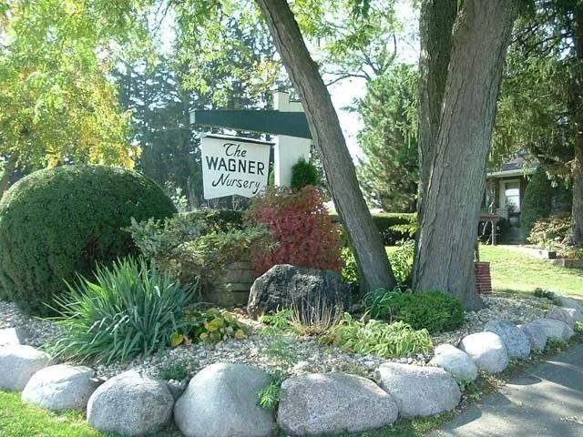 Landscaped garden with a sign reading “Wagner,” bordered by large white rocks and trees