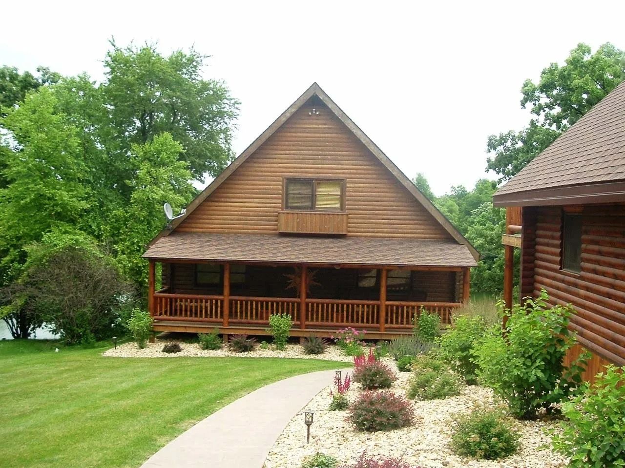 Rustic wooden cabin with porch, surrounded by green trees and a curved path through a landscaped yard