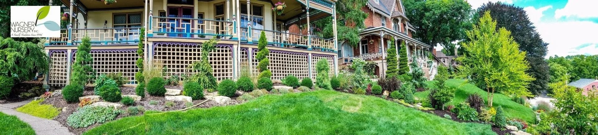 Garden and porch of a rustic house with stone steps, green lawn, and flower beds
