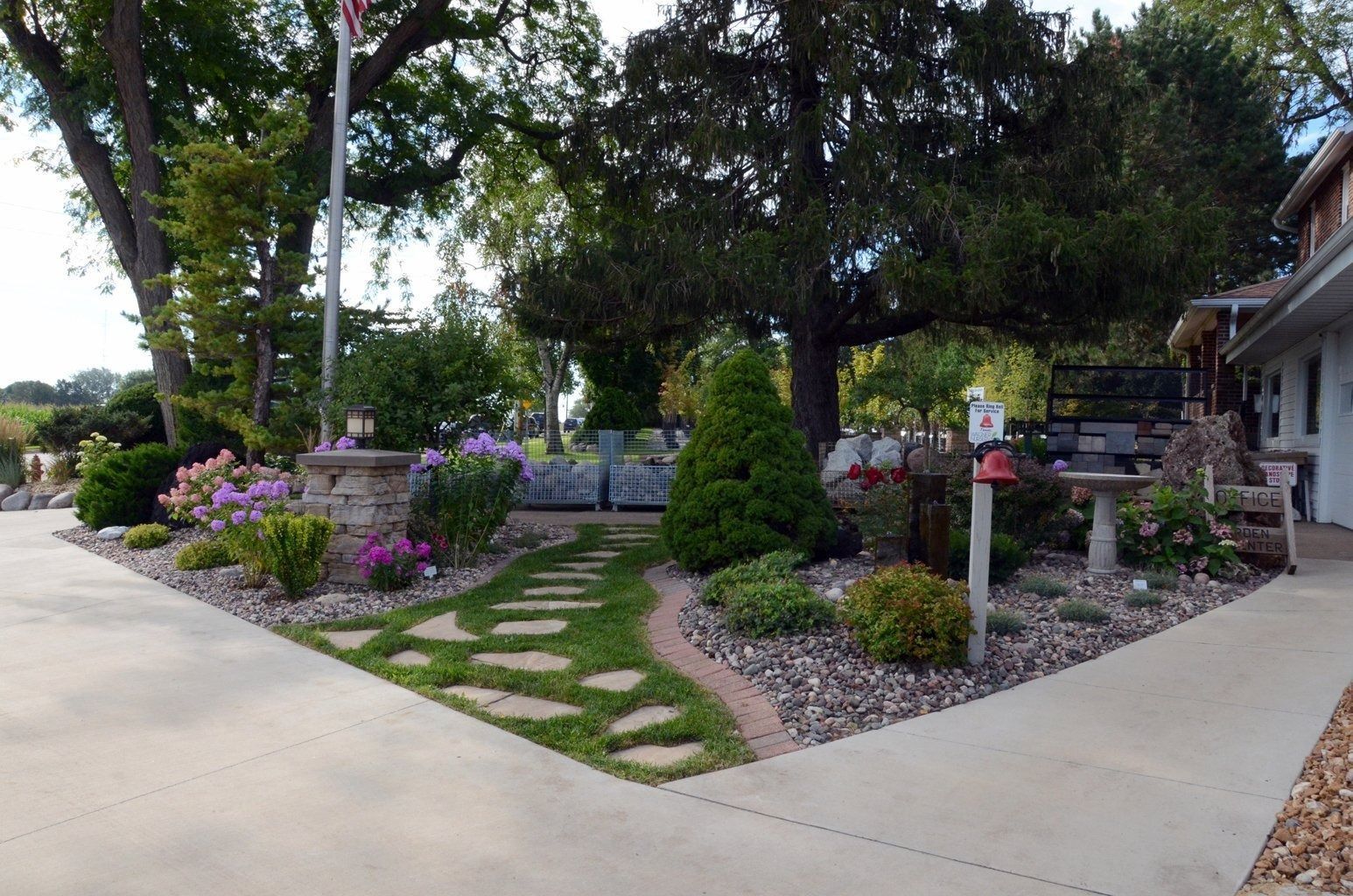 Landscaped front garden with stone path, purple flowers, trees, and a house walkway