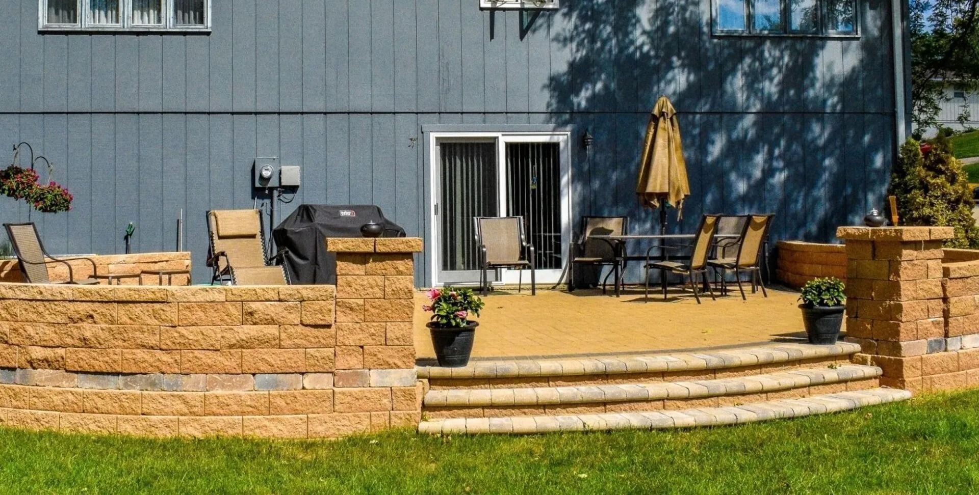 Backyard patio with stone steps, outdoor seating, and a yellow umbrella in front of a blue house