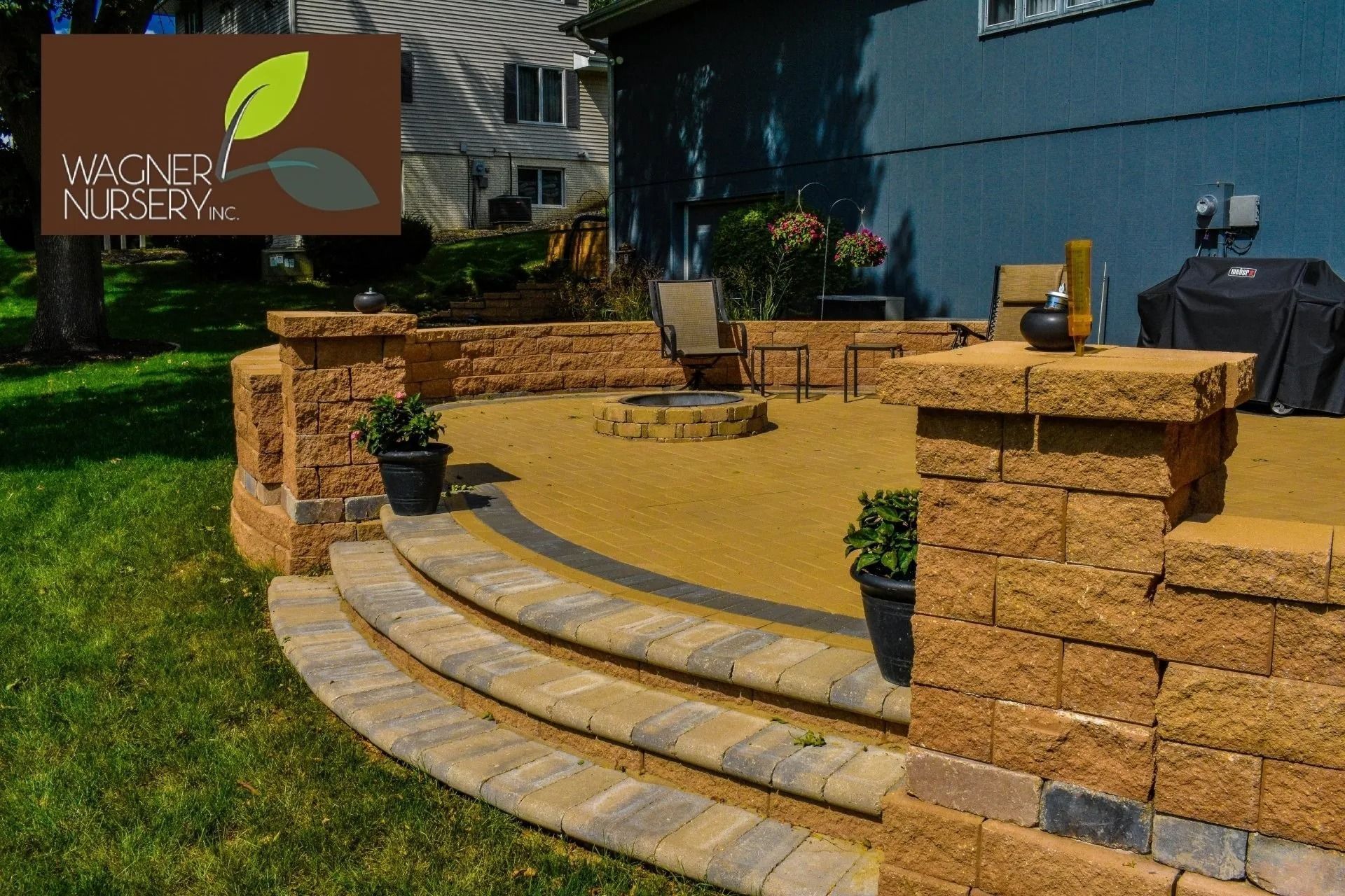 Curved stone patio steps and retaining wall in front of a blue house with a small sign and potted plants