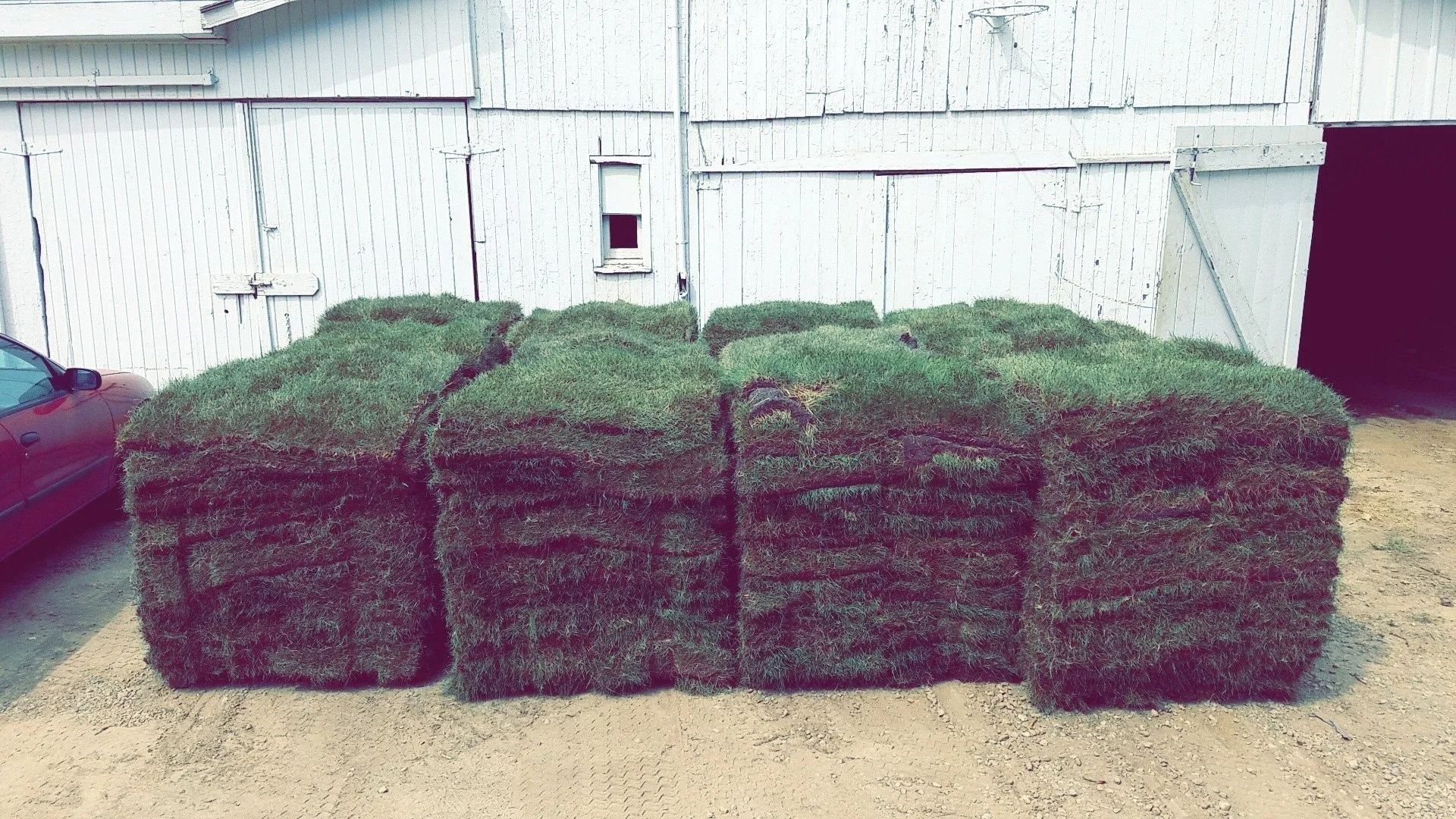 Stacked hay bales beside a white barn wall, with a concrete floor in front.