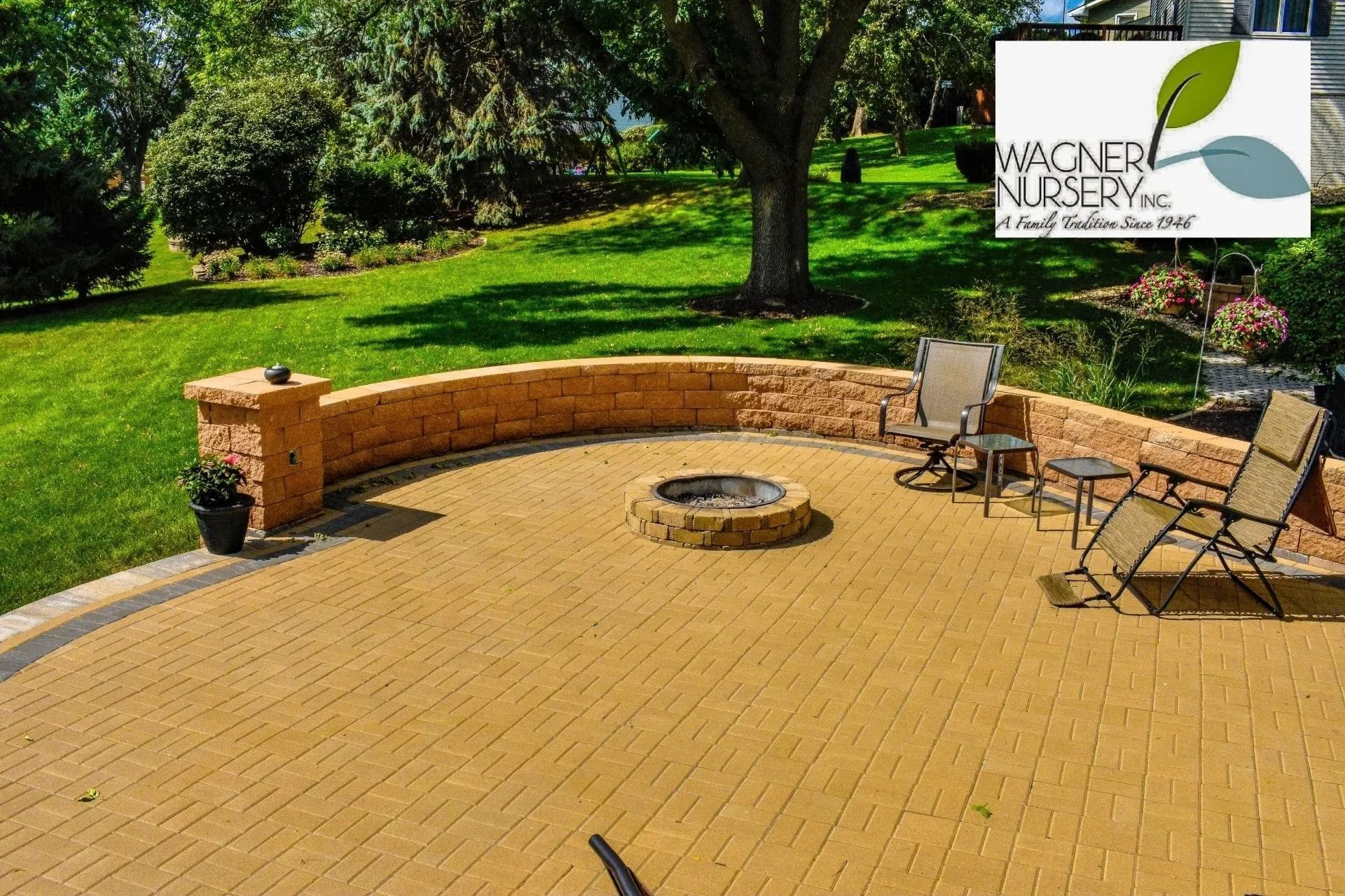 Brick patio with circular fire pit, stone bench, and two chairs in a green garden setting