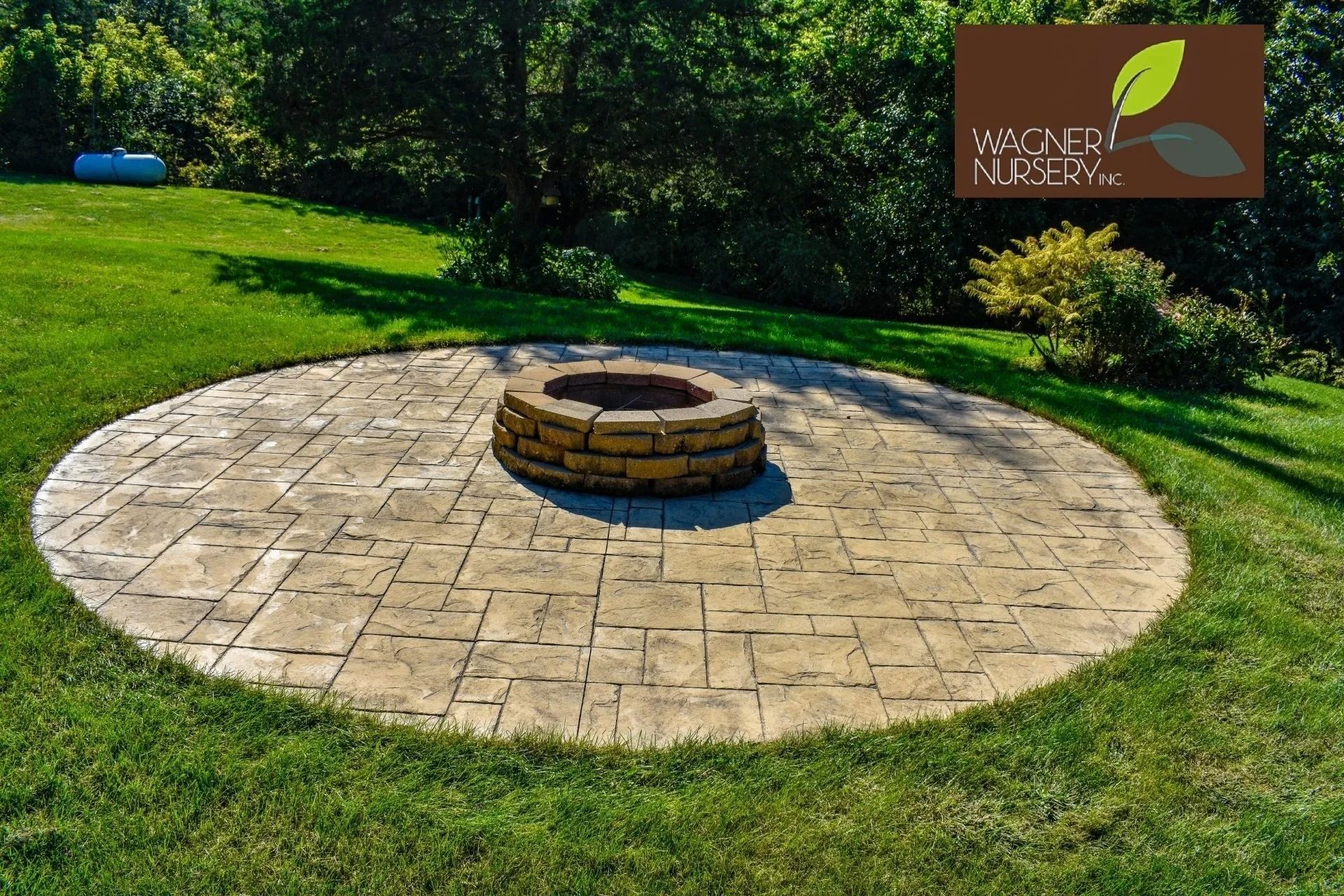 Circular stone patio with a central fire pit on a grassy lawn beside a park sign.