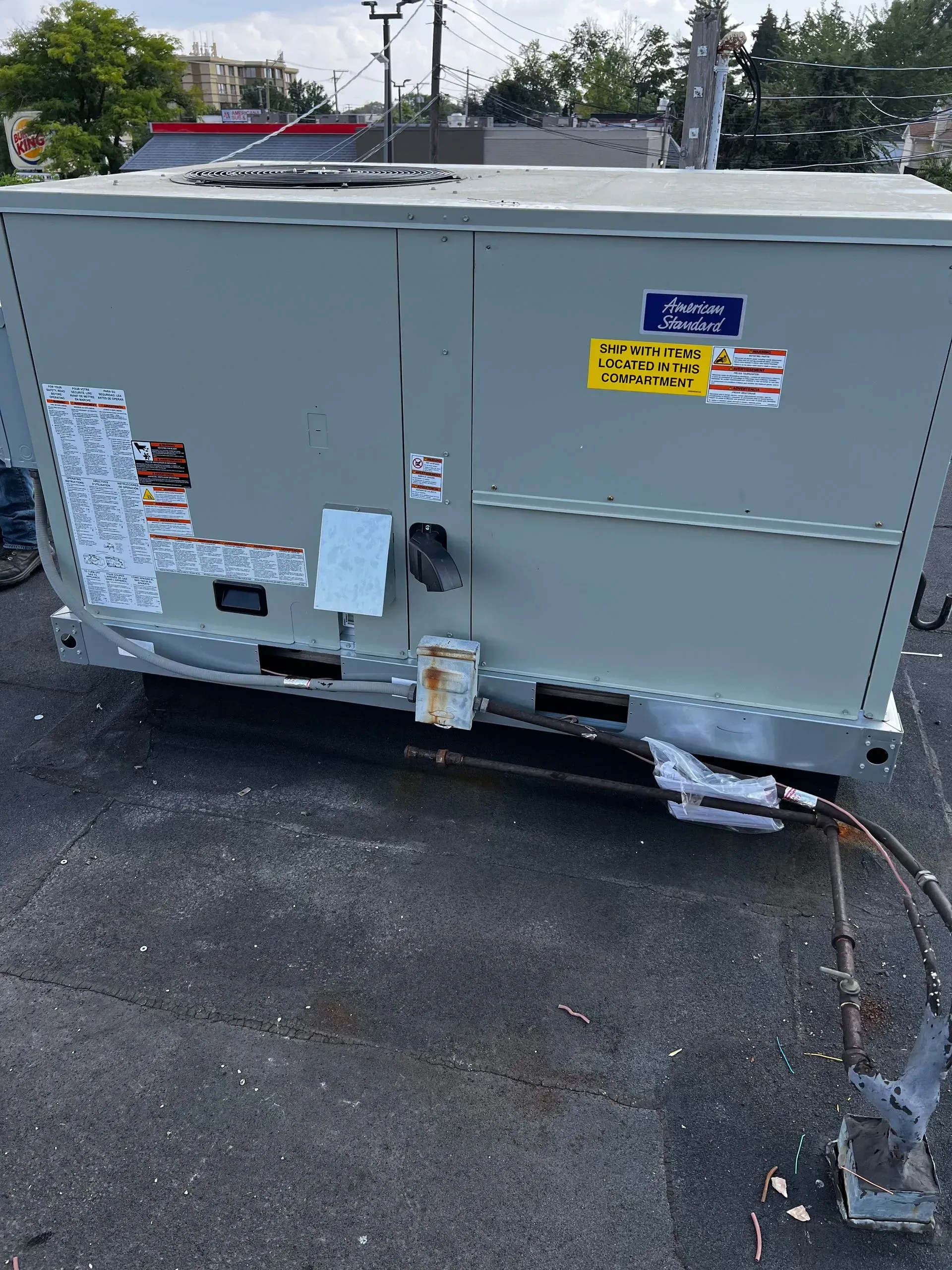 Gray HVAC unit on a flat roof with various stickers and exposed pipes.