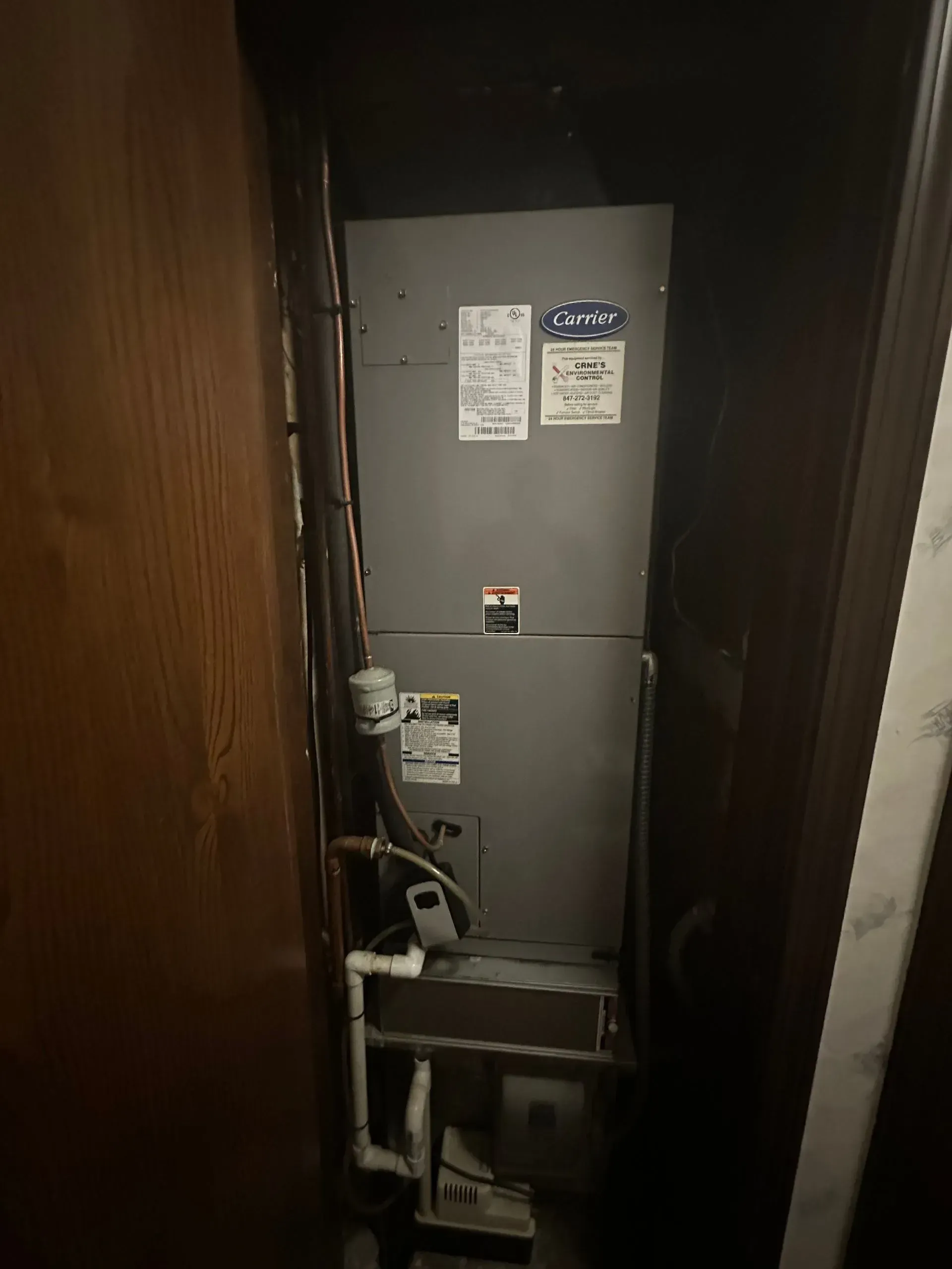 Furnace unit in a dark closet, with pipes and ductwork visible.