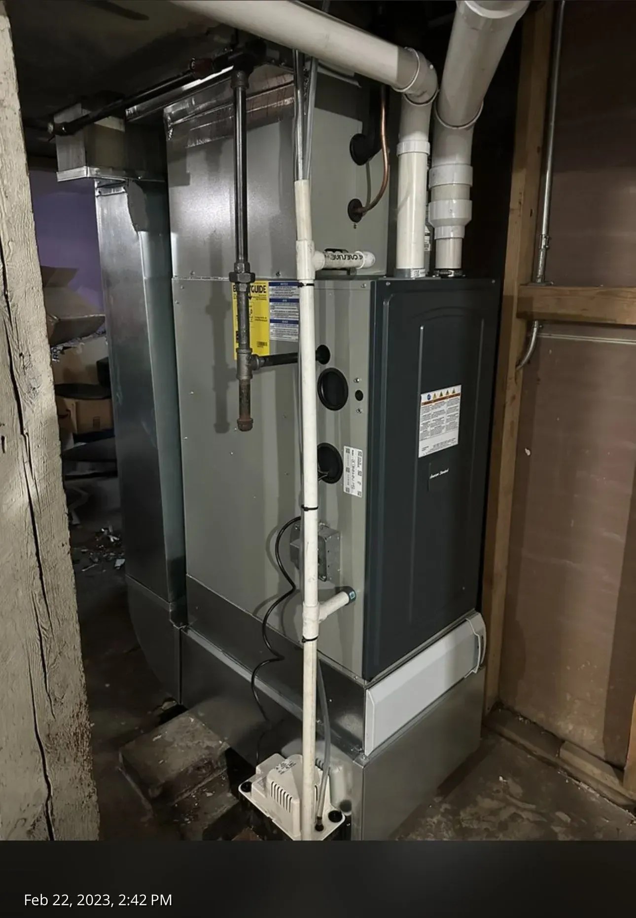 A gray furnace with white pipes in a basement setting.