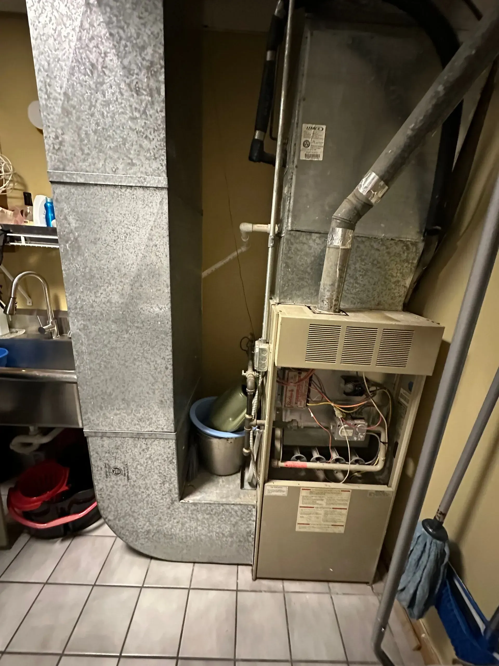 Furnace and ductwork in a utility room. Metal ducts, tan furnace, beige walls, tile floor.