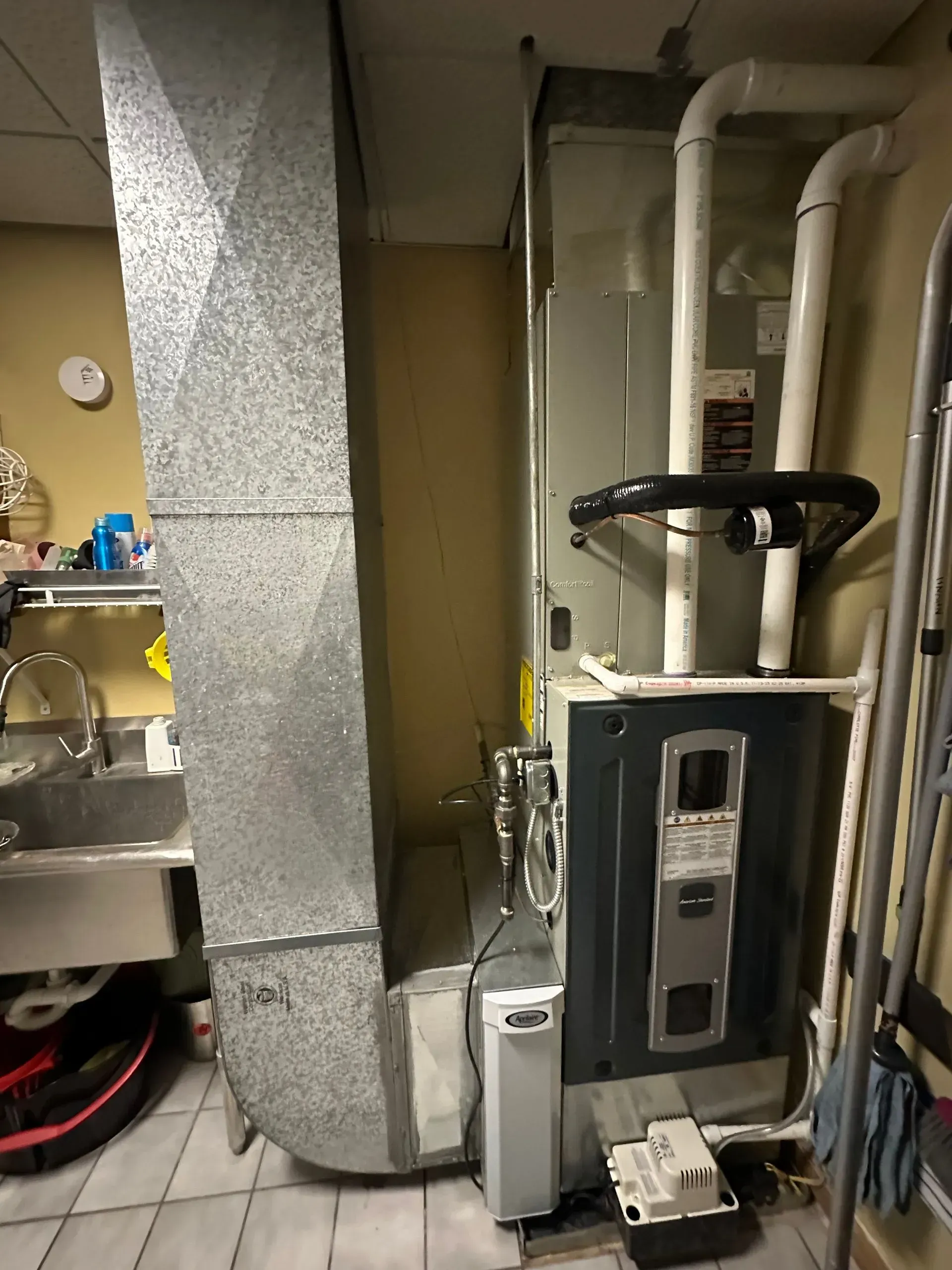 Furnace with attached ductwork, plumbing in basement. Gray metal, white pipes.