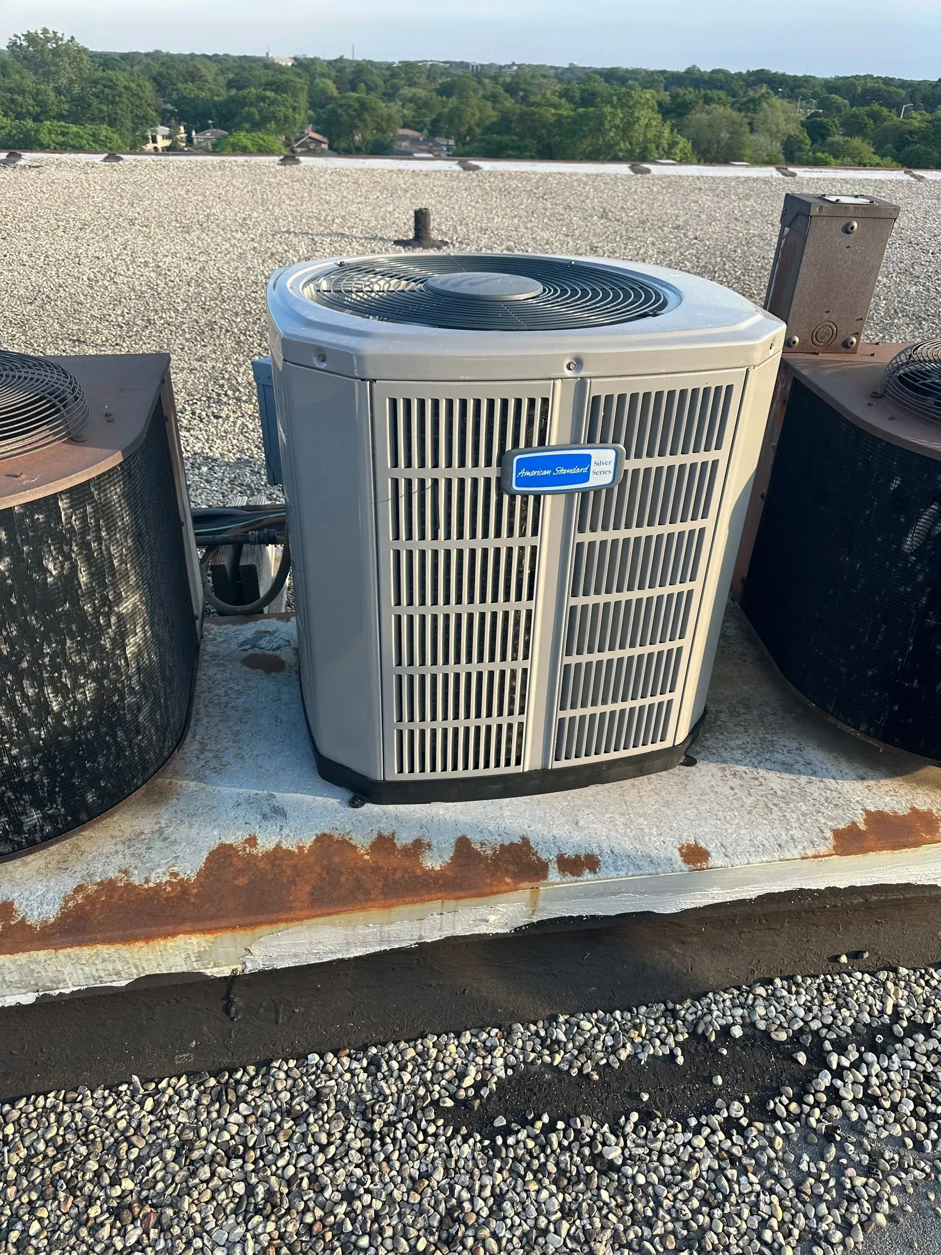 Air conditioning unit on a rooftop with gravel and metal structures, under a cloudy sky.