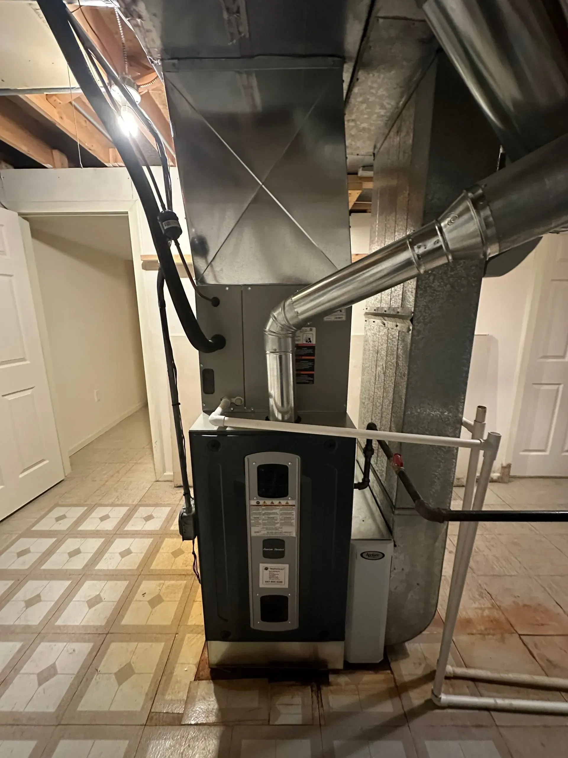 Furnace in a basement with ductwork, pipes, and a white door in the background.