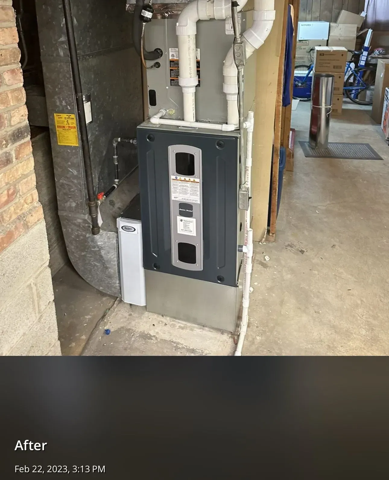 Furnace in a basement; grey and black unit against a concrete wall; white pipes and ducts.