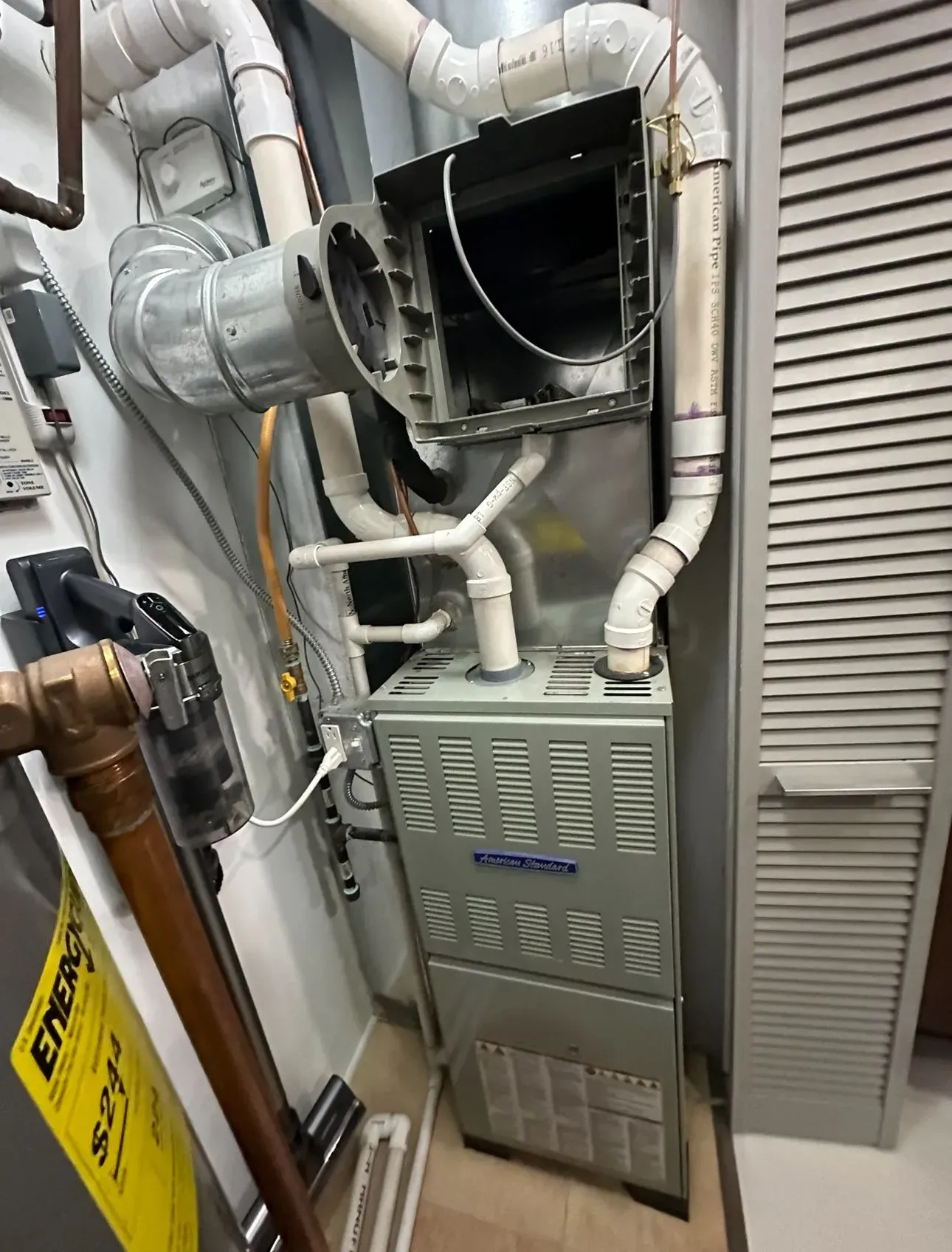 Furnace in a utility room with ductwork, pipes, and a vent. Gray, white, and beige colors.