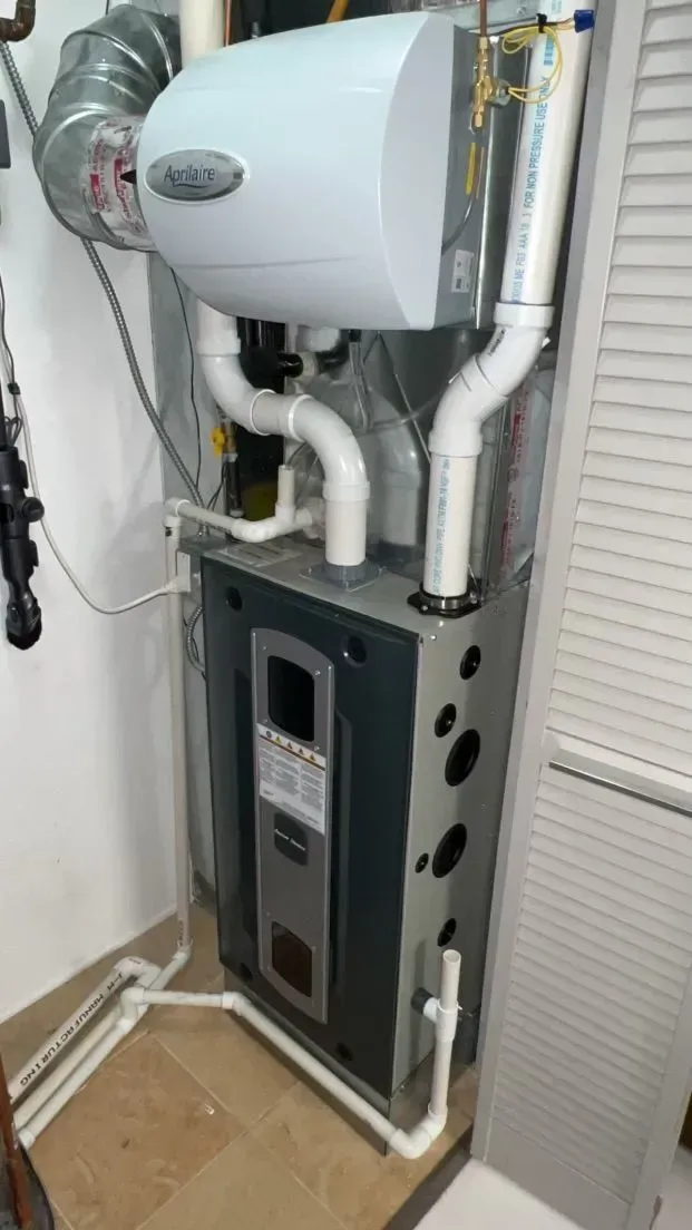 Furnace with humidifier attached; white and gray, pipes visible. Located in a utility room, near a white door.