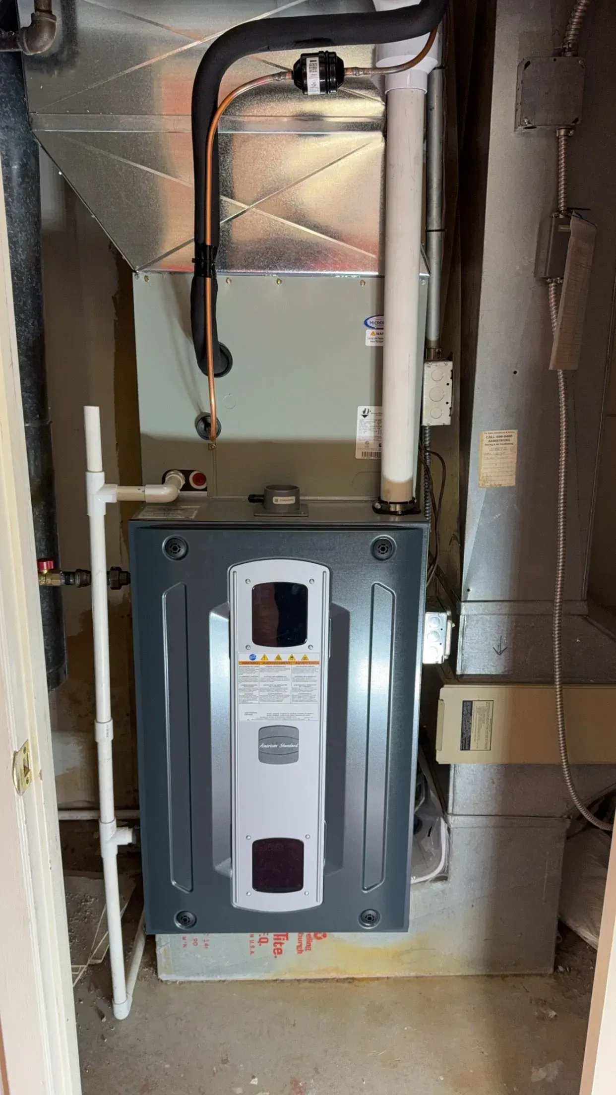 Furnace with gray exterior, white pipe, and black tube in a utility room.