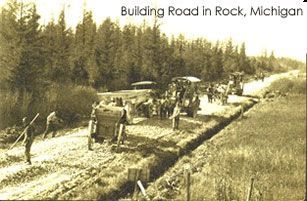 Road construction in Rock, Michigan, with workers and machinery, circa early 20th century.