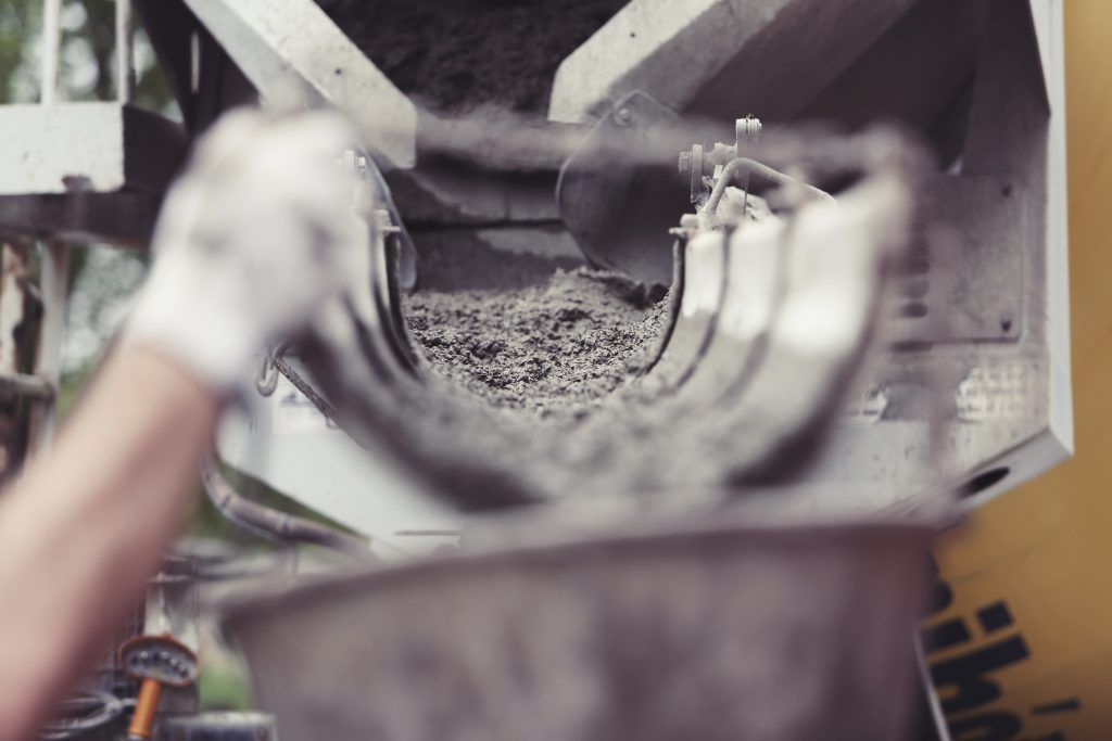 Hand in white glove with a cement mixer depositing concrete into a bucket.
