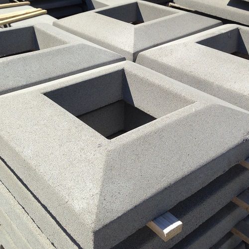 Stacked gray concrete post caps with square openings.