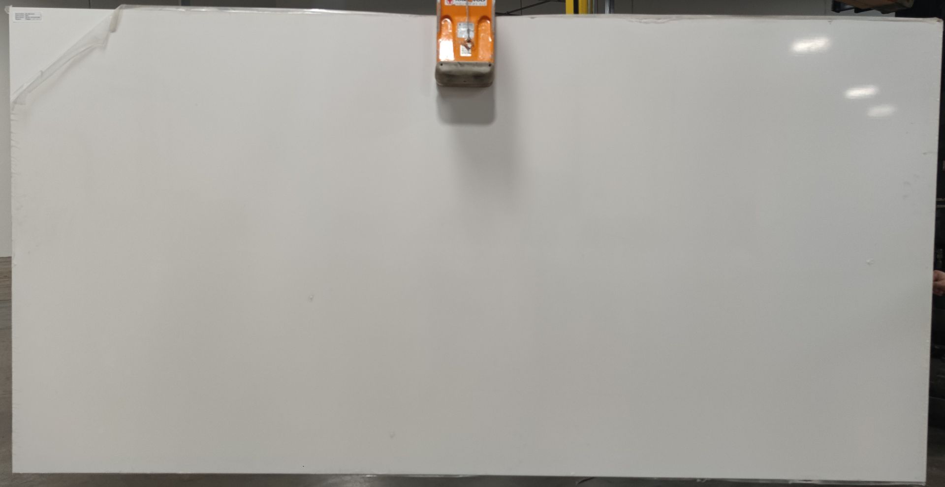 A large white board is hanging from a crane in a warehouse.